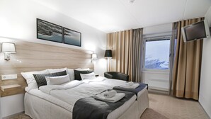 A hotel room with a large bed, two bedside tables, a flat-screen TV, and a window with curtains. - Hotell Fjället (Björkliden)
