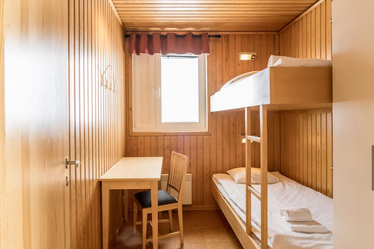 A small, wooden room with bunk beds, a desk, and a chair.