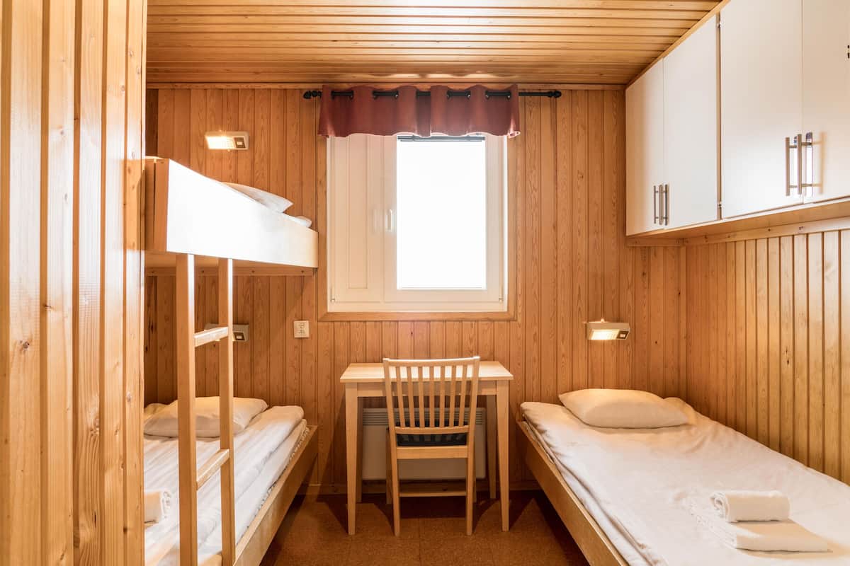 A wooden cabin room with bunk beds, a desk, and a window.