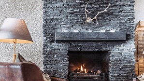A cozy living room with a stone fireplace, leather sofas, and a table with a glass. - Hotell Fjället (Björkliden)