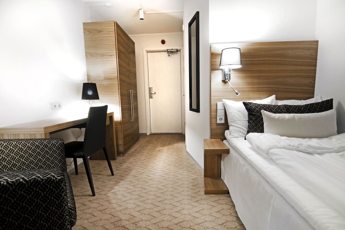 A hotel room with a bed, a desk, a chair, and a wardrobe.