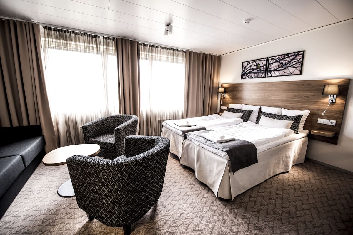 A hotel room with a large bed, two armchairs, a small round table, and a sofa.