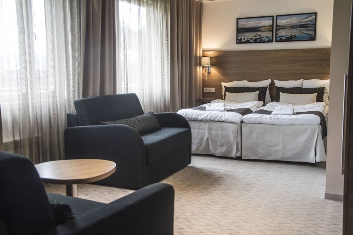 A hotel room with a bed, two bedside tables, a sofa, a small round table, and a window with curtains.