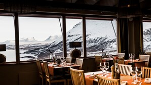 A restaurant with tables set for dining, large windows offering a view of snow-covered mountains. - Hotell Fjället (Björkliden)