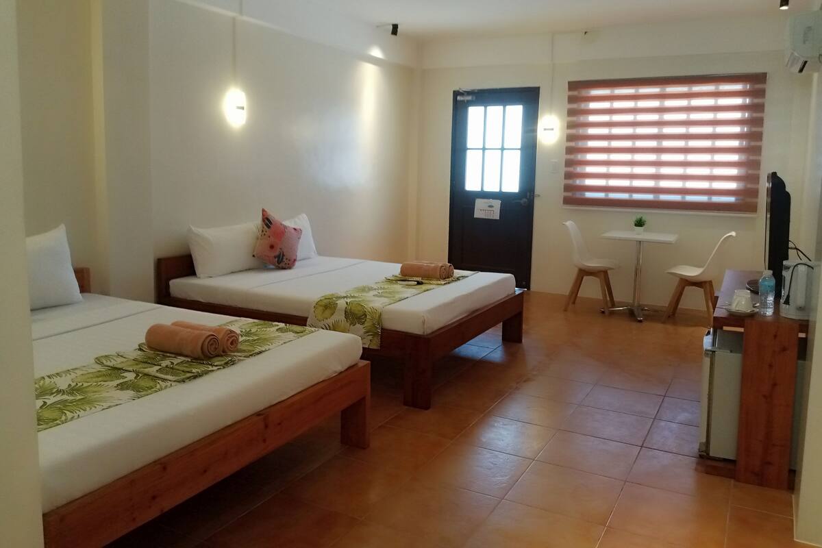 Une chambre d’hôtel avec deux lits simples, un petit bureau, une chaise et un téléviseur.