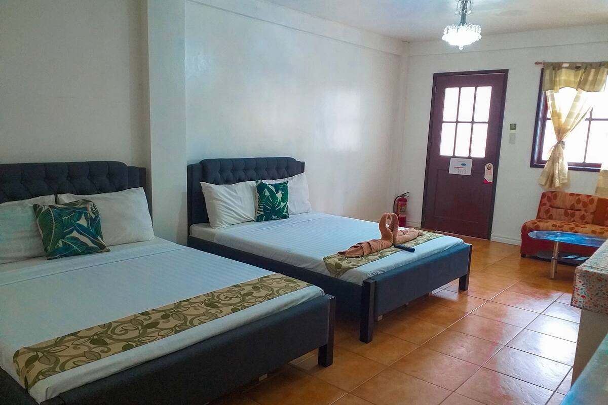 Une chambre d’hôtel avec deux lits, un canapé, une petite table et une porte avec une fenêtre.