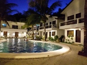 A swimming pool surrounded by multi-story buildings with balconies, palm trees, and a paved walkway. - Feliness Resort Boracay (Boracay Island)