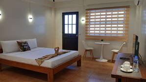 Ein Hotelzimmer mit einem Bett, einem Schreibtisch mit Stuhl, einem kleinen Tisch mit Pflanze und einem Fenster mit Jalousien.
