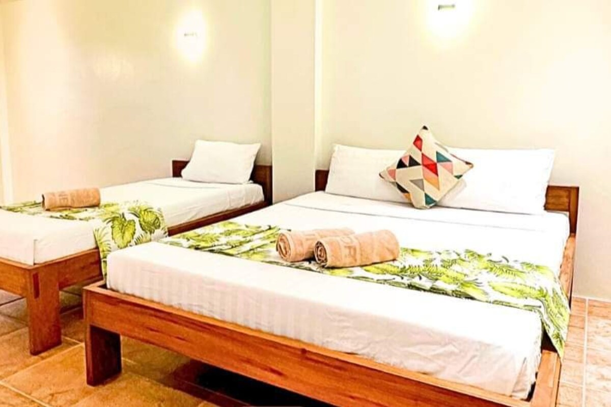 Habitación de lujo con dos camas de madera, cada una con ropa blanca y colcha estampada con hojas verdes.