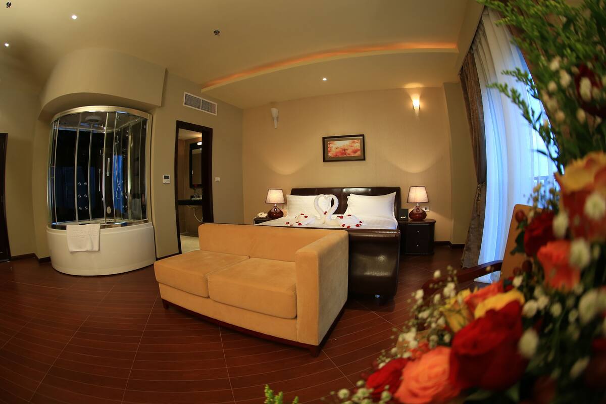 A hotel room with a curved ceiling, a jacuzzi, a sofa, a bed with a white headboard, and a nightstand with lamps.