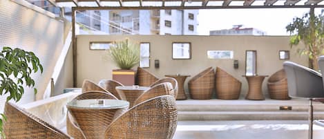 Wicker chairs and a glass table on a tiled patio with a sofa and cushions in the background.