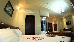 A hotel room with a large bed, a desk, a chair, a TV, and a bathroom with a mirror and sink. - Magnolia Addis Hotel (Addis Ababa)