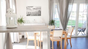 A dining area with a wooden table and chairs, a white cabinet with jars, and a black and white landscape painting on the wall.