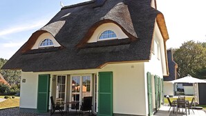 A house with a steeply pitched roof, green shutters, and a patio with outdoor furniture.