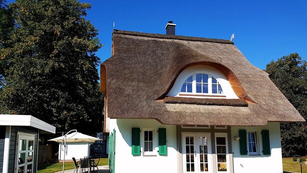 A traditional house with a thatched roof, a small porch, and a well-maintained lawn.