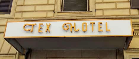 Ein Hotel Schild mit dem Schriftzug "CEX HOTEL" in goldener Schrift auf weißem Grund.