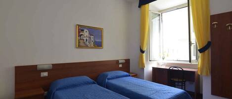 Habitación de hotel con dos camas individuales, un escritorio, una silla y una ventana con cortinas amarillas.