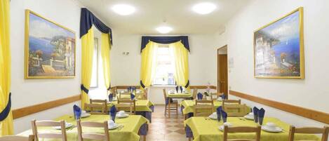 A dining area with tables set for service, yellow tablecloths, and blue chair covers.