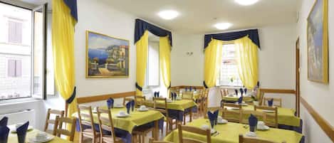 A dining area with multiple tables set for guests, featuring yellow tablecloths and blue accents.