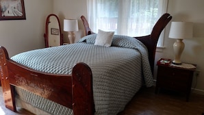 Una cama bien hecha con cubrecama acolchado, cabecera de madera, dos lámparas de noche y una mesita con una caja.
