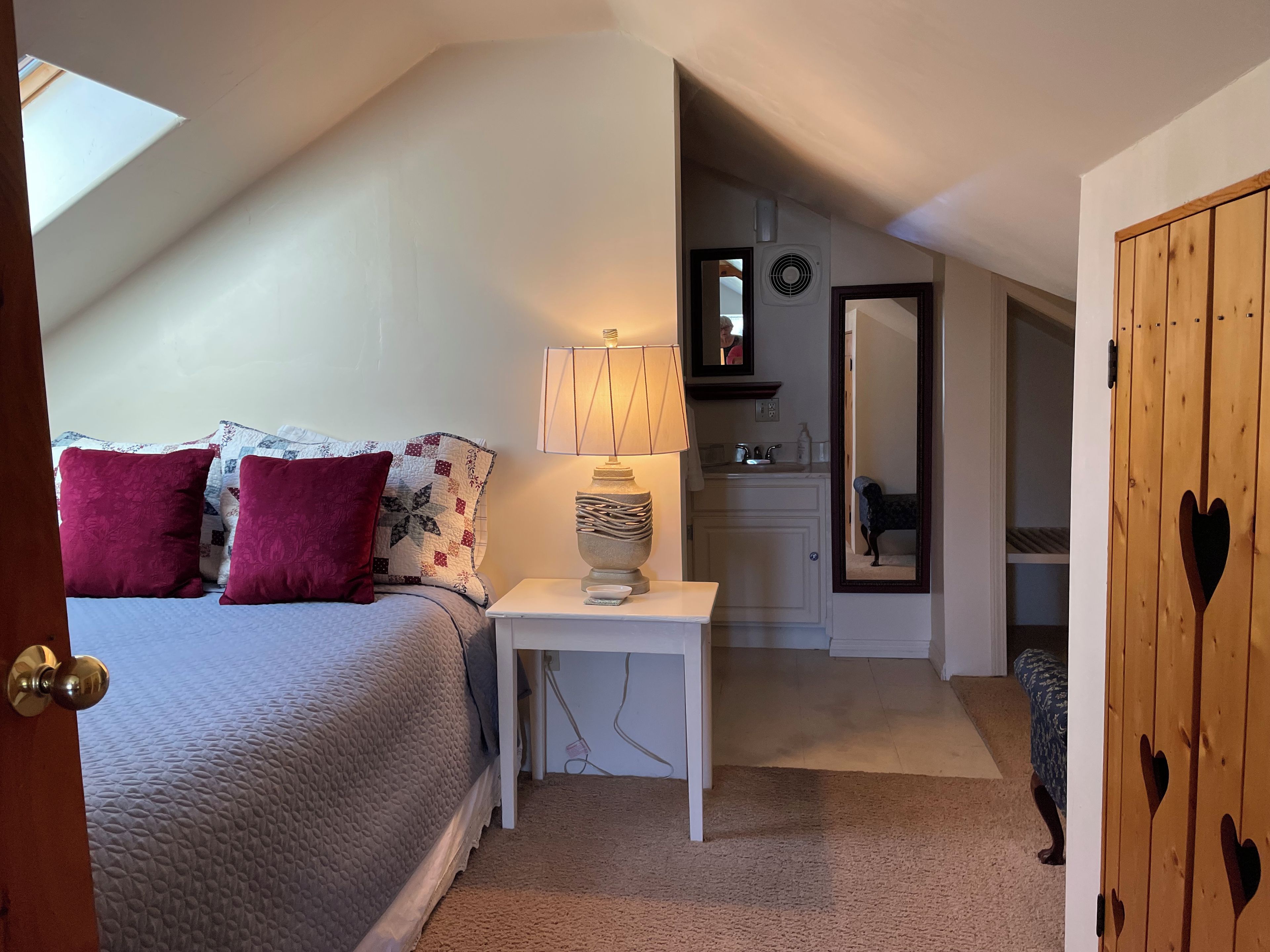 A bedroom with a bed, bedside lamp, and a view into a bathroom.