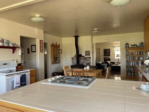 A kitchen with a gas stove, oven, and a brick wall. There is a dining area with chairs and a table, and a bookshelf filled with books.