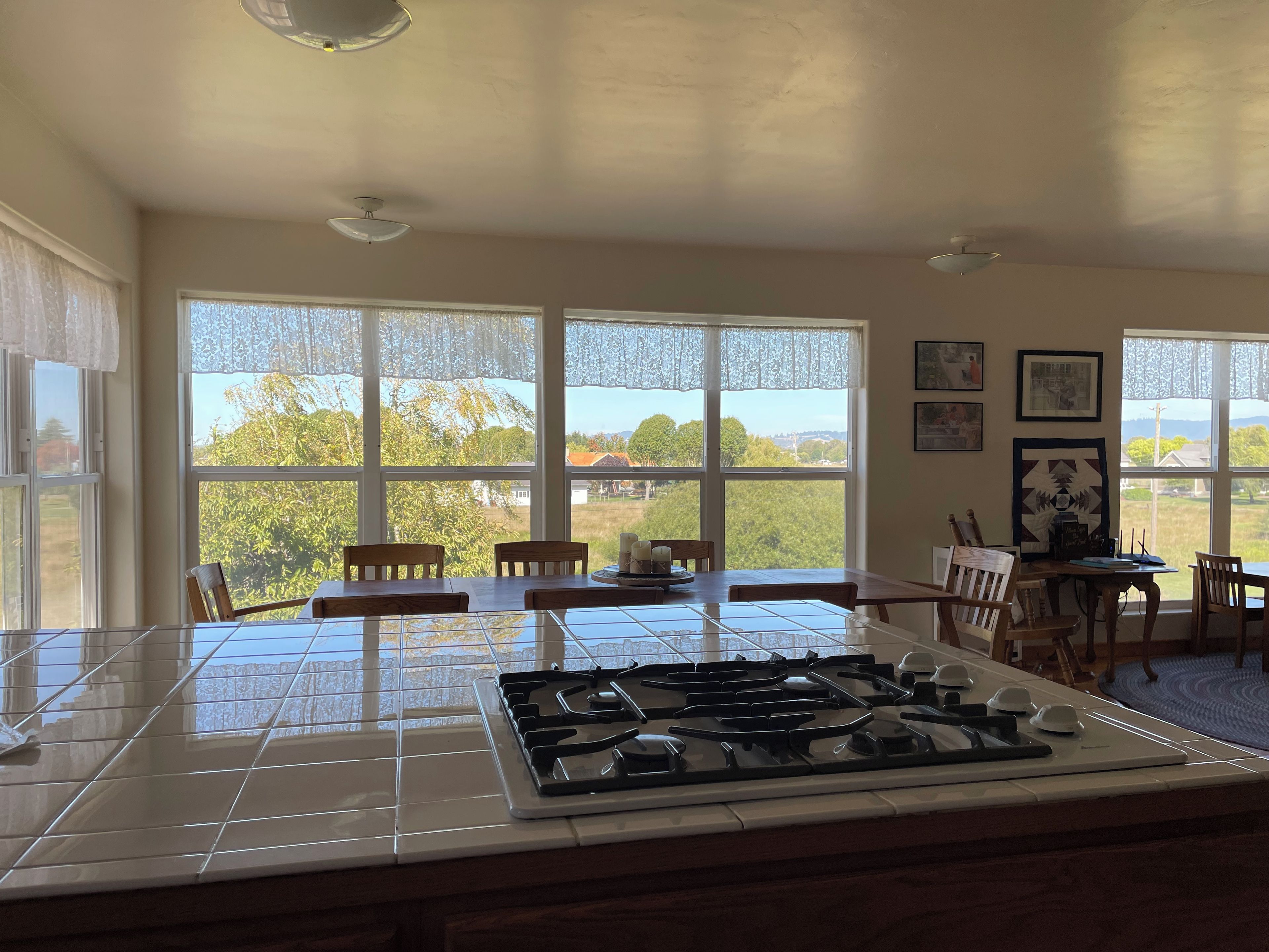 A kitchen with a gas stove, dining table, chairs, and large windows offering a view of greenery and buildings.