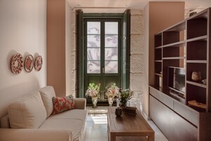 A living room with a sofa, coffee table, and decorative vases. There is a green door with glass panels and a bookshelf with various items.