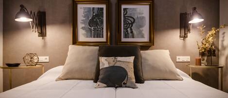 Una cama bien hecha con dos almohadas, un cabecero y una mesita de noche con una lámpara y un florero.