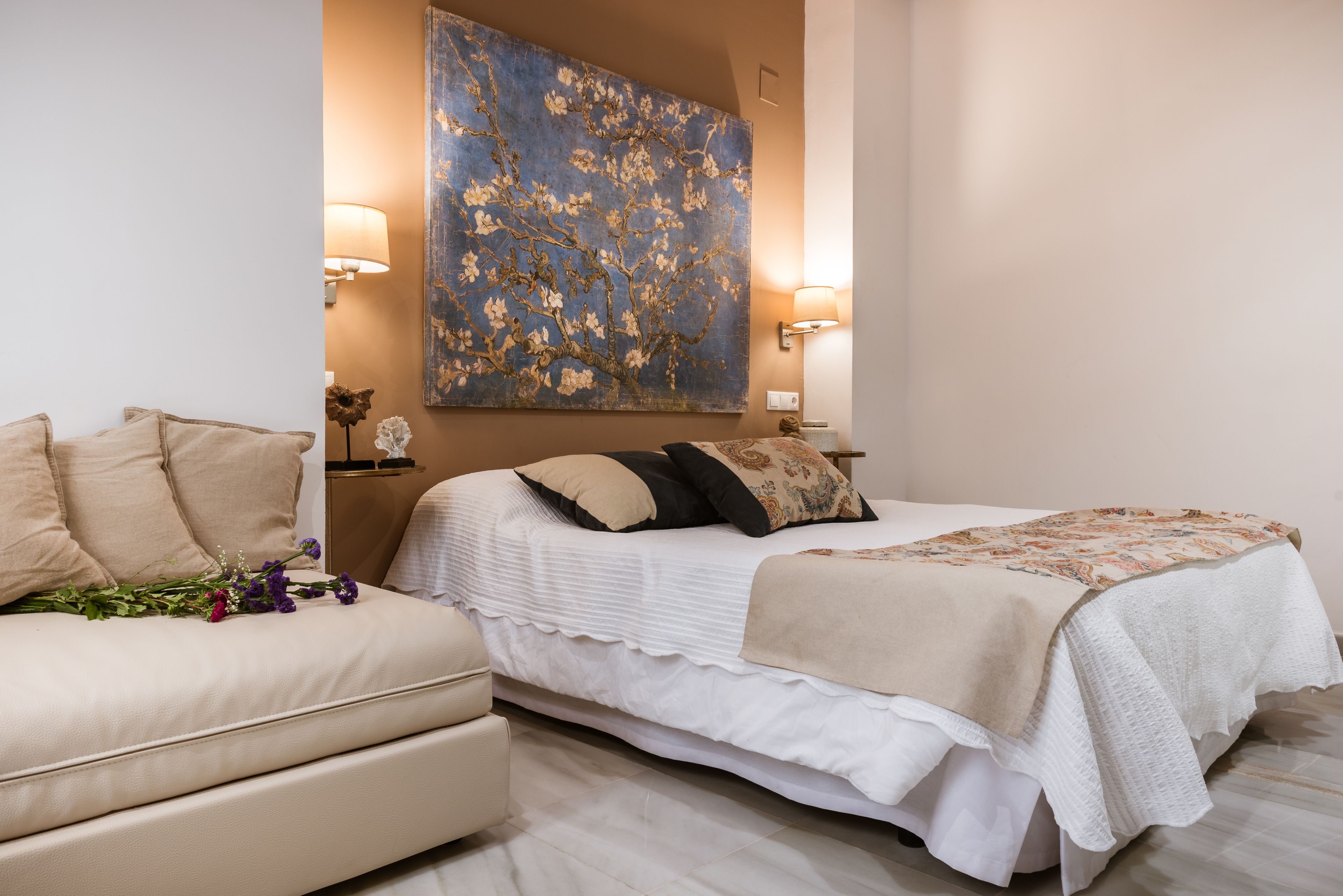 A bedroom with a bed, a sofa, and a large floral painting on the wall.