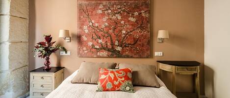 A bedroom with a bed, two bedside tables, a nightstand, a vase with flowers, and a wall-mounted painting.