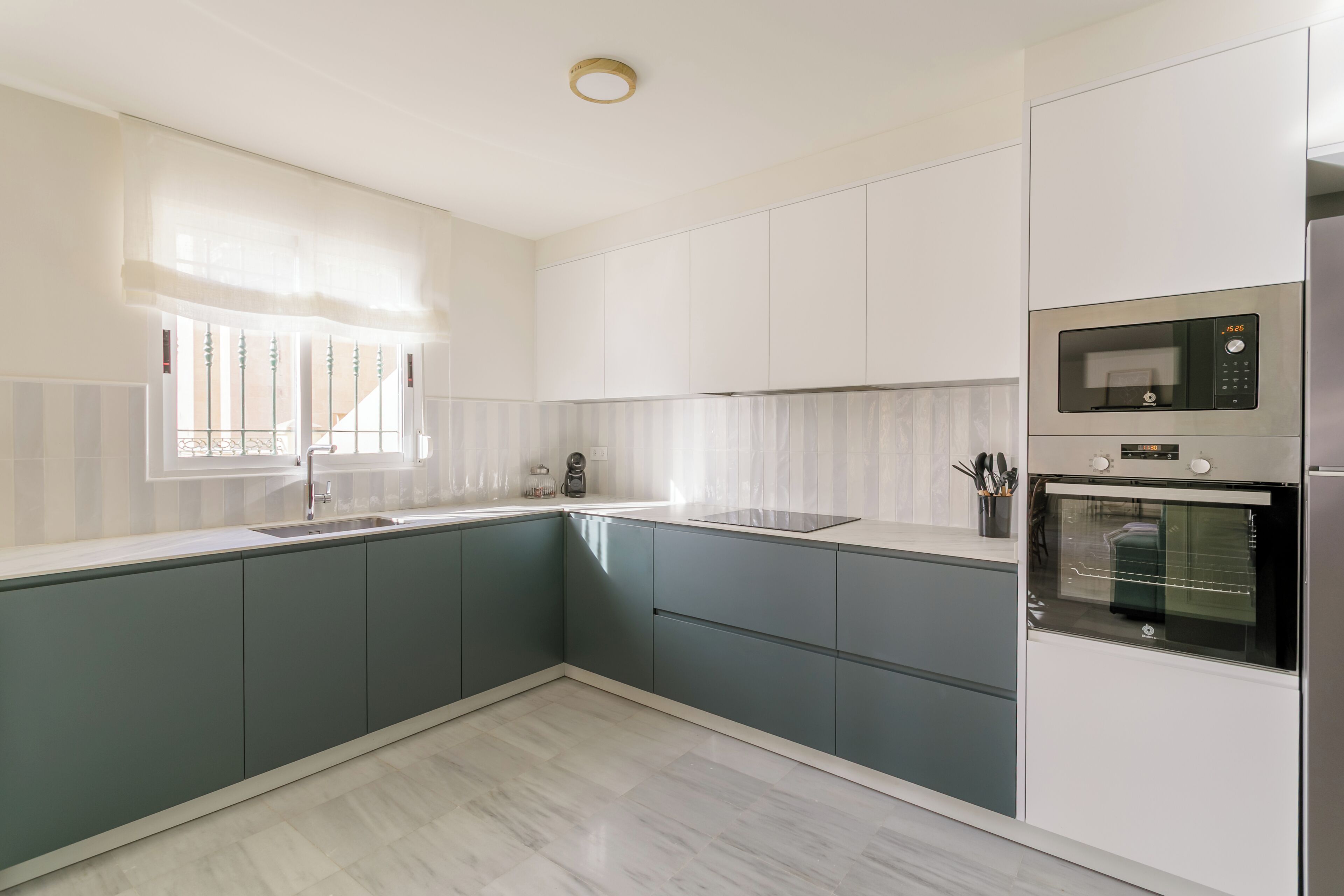 Cozinha moderna com pia, micro-ondas, forno e janela com cortinas leves.