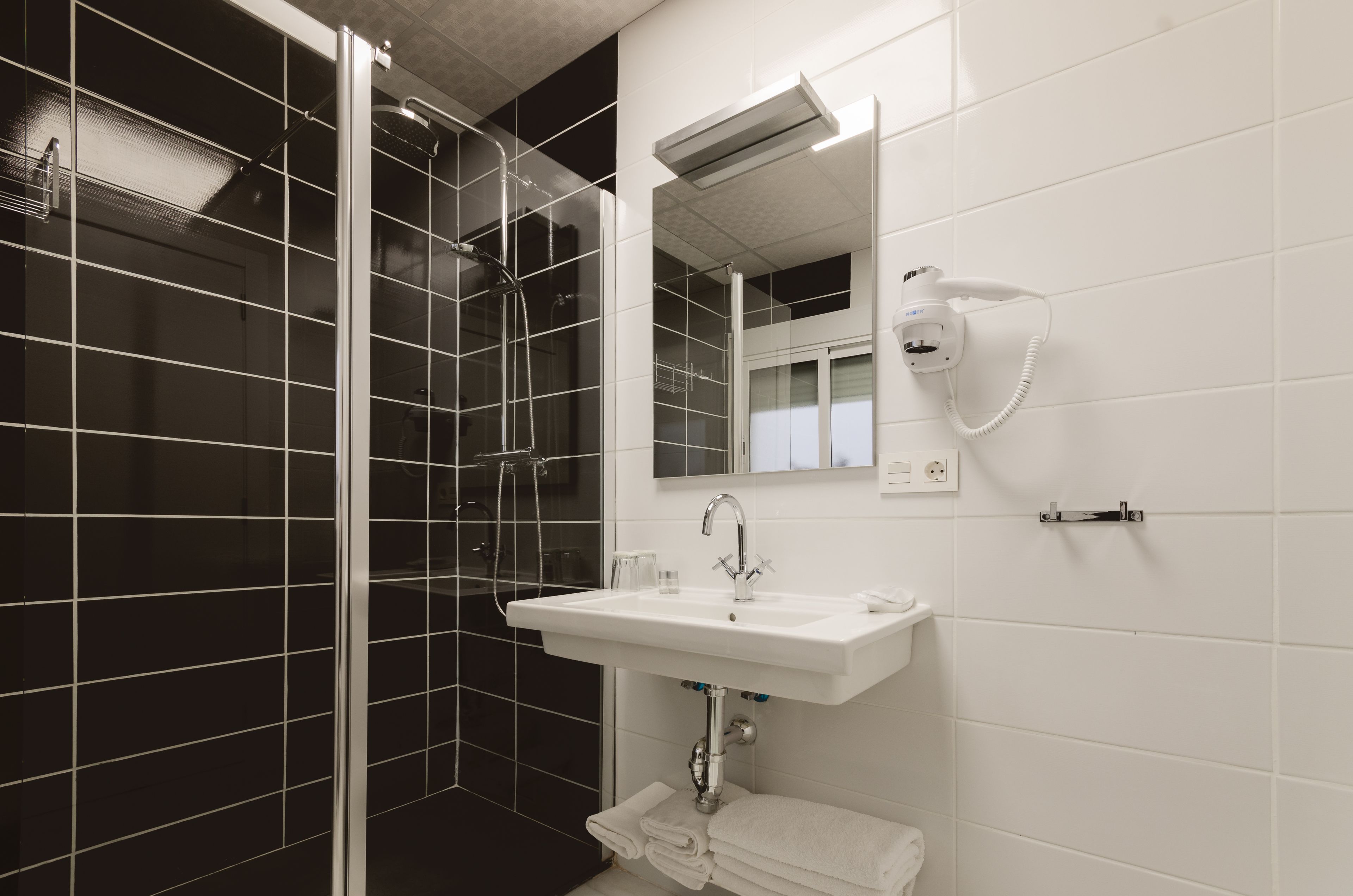 A modern bathroom with a glass-enclosed shower, a white sink, and a hairdryer mounted on the wall.