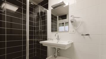 A modern bathroom with a glass-enclosed shower, a white sink, and a hairdryer mounted on the wall.
