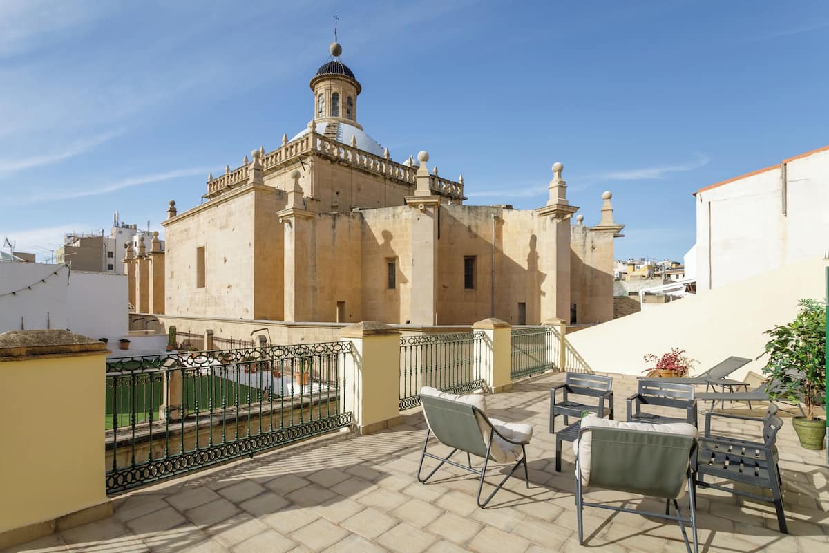 A rooftop terrace with outdoor furniture, a view of a historic building with a dome and bell tower, and a clear sky.