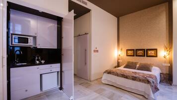 Un dormitorio con cama, mesita de noche, televisor montado en la pared y una zona de cocina con microondas.