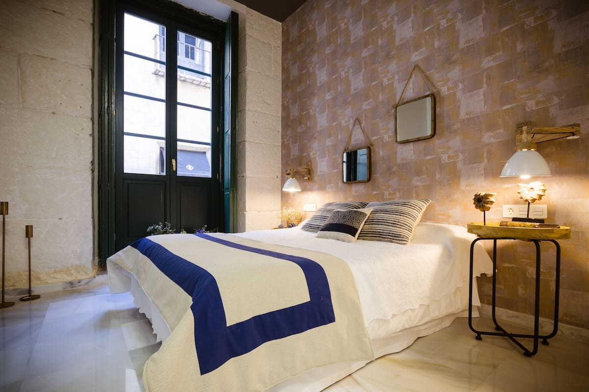 A bedroom with a bed, a nightstand, a mirror, and a door.