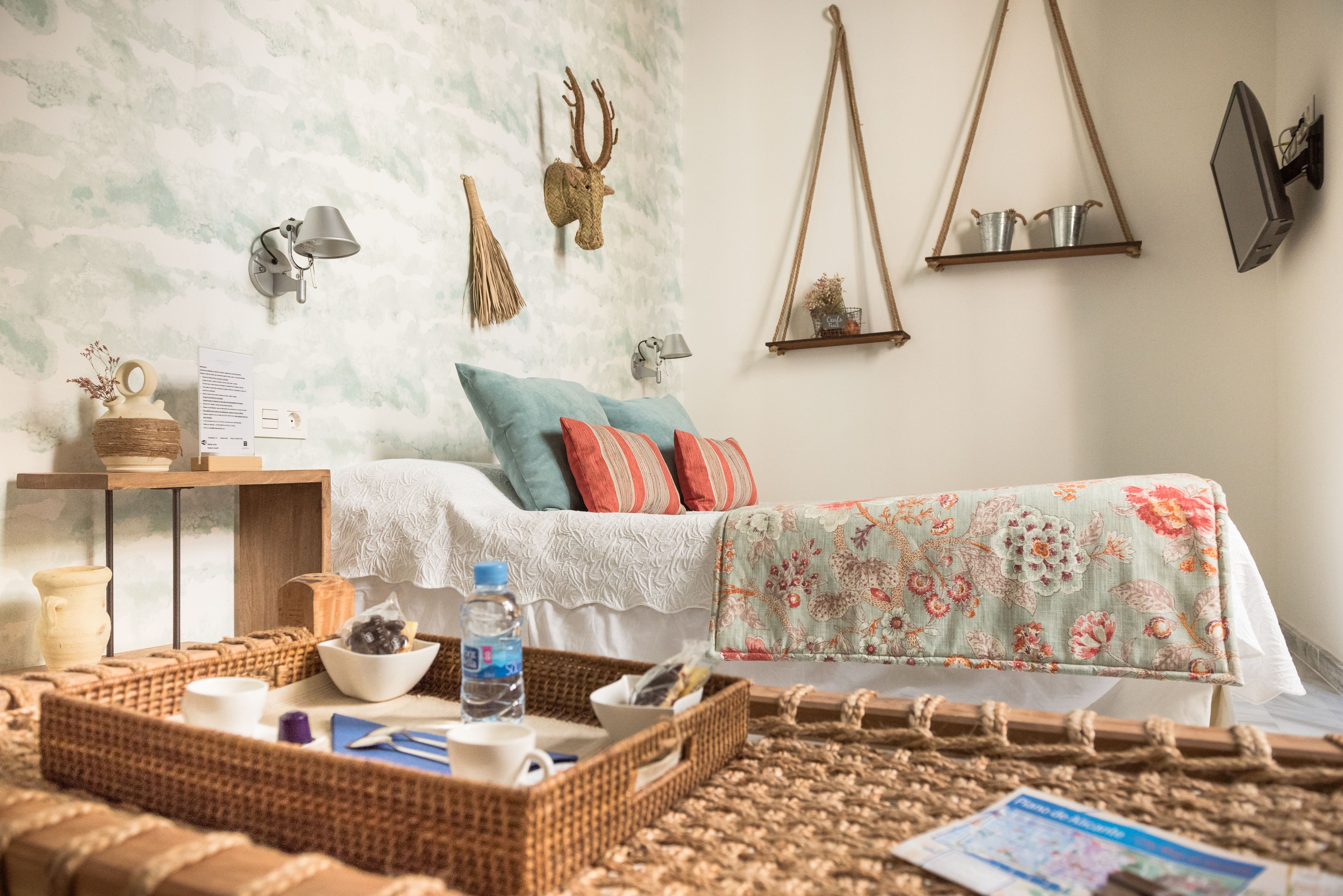 Un dormitorio acogedor con cama, una mesita de noche, una lámpara de pared, un ciervo decorativo como adorno y una estantería colgante con plantas.