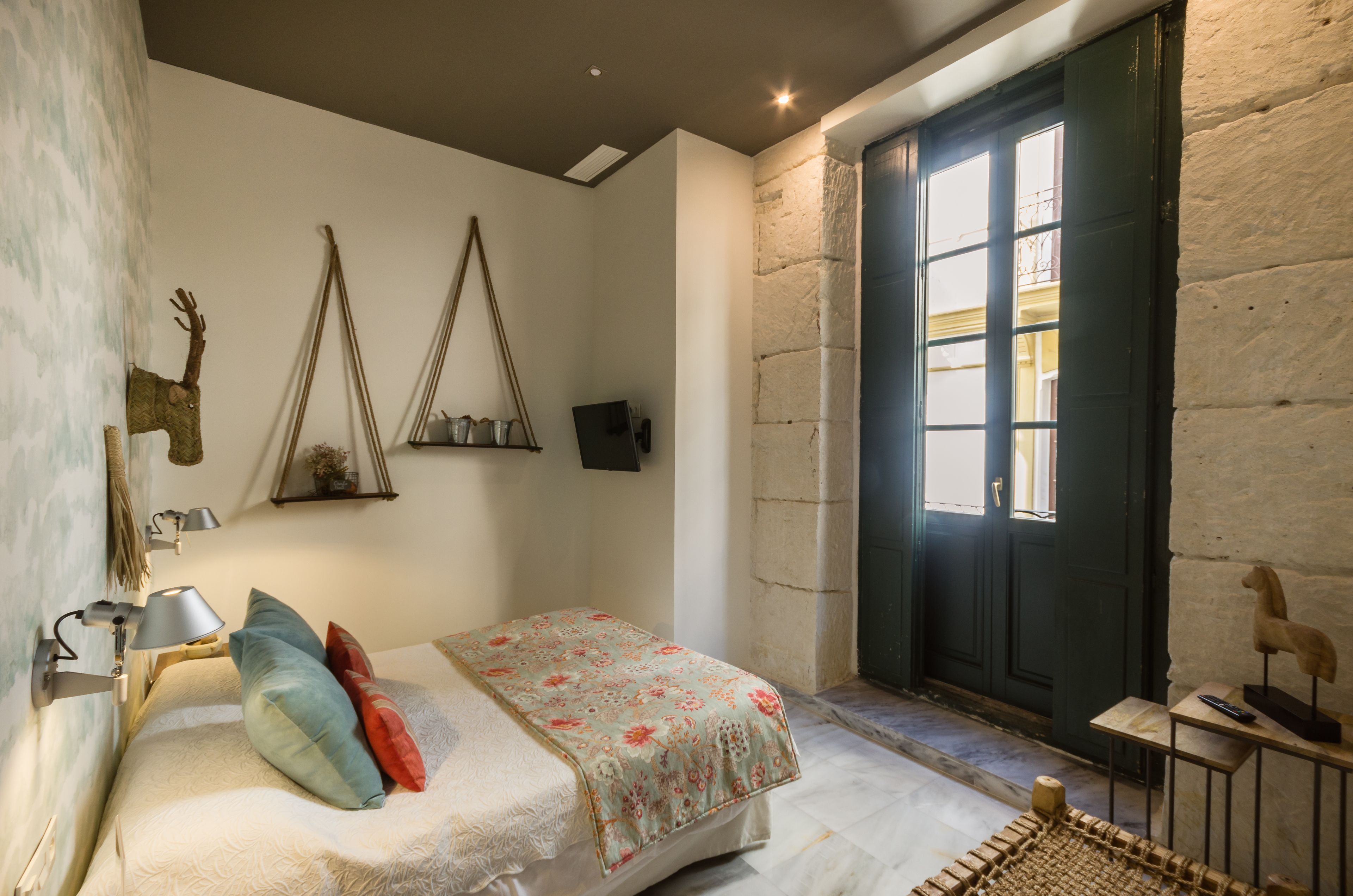 Ein Schlafzimmer mit Bett, Schreibtisch, Lampe und einem Fenster mit Blick ins Freie.