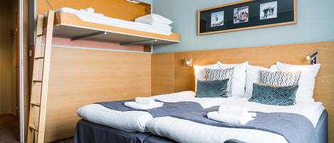 A hotel room with a bunk bed, a desk, and a headboard with a shelf.