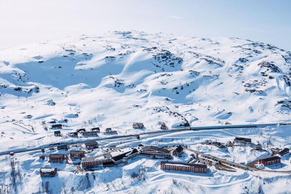 A snow-covered mountain with a small town at its base, featuring several red-roofed buildings and a train track running through the area.