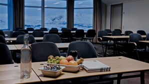 Un salón de conferencias con mesas y sillas, una botella y una bandeja de frutas.