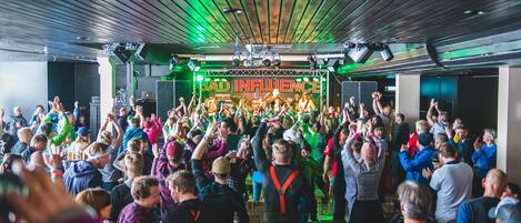 Un evento multitudinario en interiores, con un escenario y un letrero de neón que dice 'BAD INFLUENCE'.