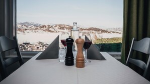 Una mesa dispuesta con saleros, pimenteros, una botella y copas de vino tinto, con vistas a una montaña nevada a través de una ventana.