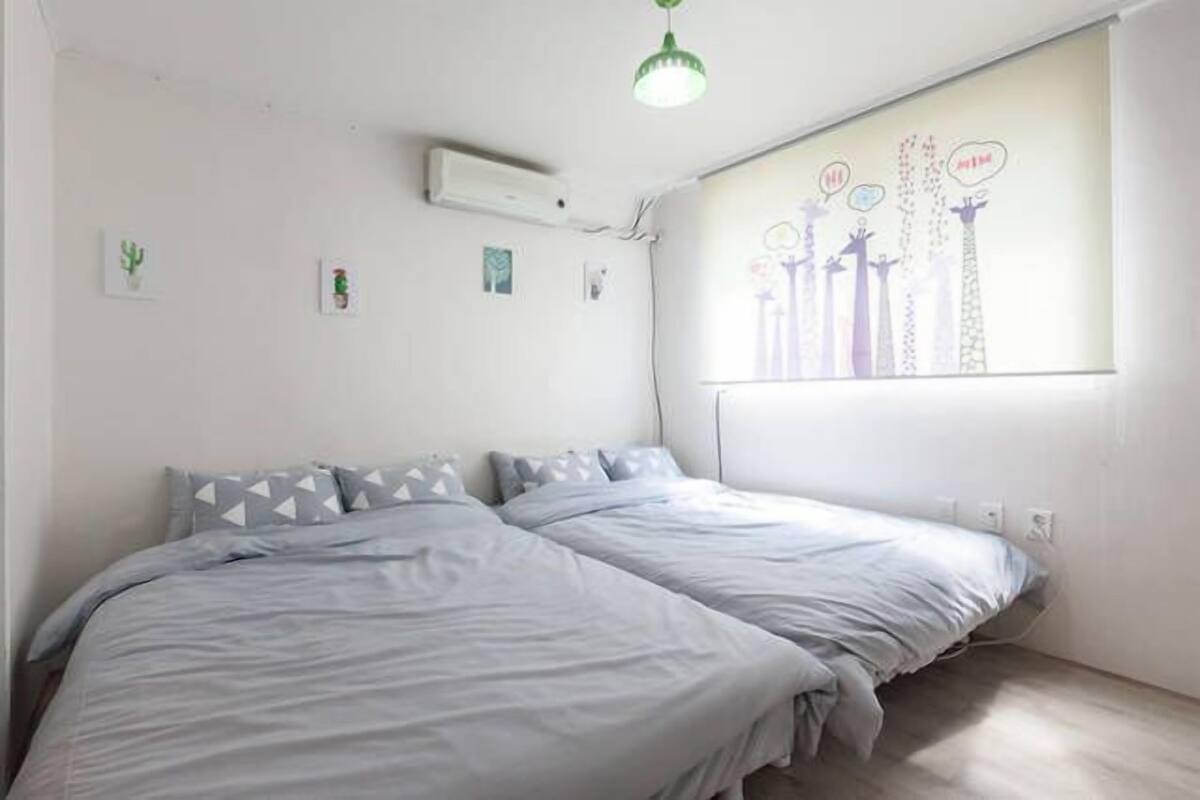 Ein Schlafzimmer mit zwei Betten, einem Fenster mit Stadtbild-Wandgemälde und einem Deckenventilator.