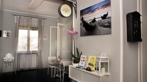 A room with a clock, a painting of a boat on a beach, a plant, and a small table with chairs. - B&B Binario Uno (Taranto)