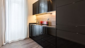 A modern kitchen with dark cabinetry, a wooden countertop, and a red toaster. - Letheshome Apartments (Porto)