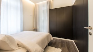 A modern bedroom with a bed, dark wardrobe, and a light-colored rug. - Letheshome Apartments (Porto)