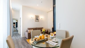 A modern dining area with a glass table, beige chairs, and a breakfast setting including oranges and pastries. - Letheshome Apartments (Porto)