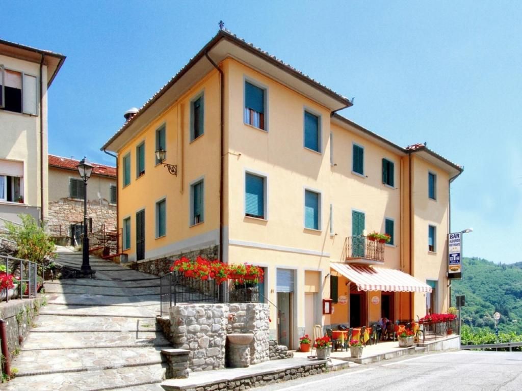 Un edificio a due piani con un bar al piano terra, scale in pietra che conducono all'ingresso e uno sfondo di vegetazione.
